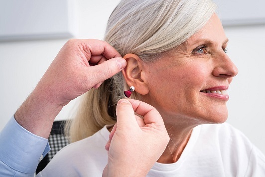 Ältere Frau bekommt Hörgerät angepasst, Hörakustiker setzt Hörhilfe am Ohr ein.